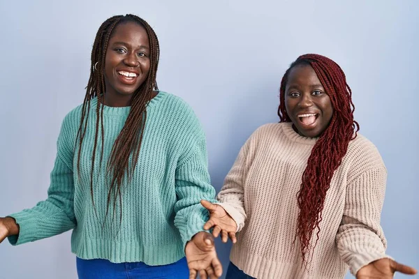 Две Африканки Стоящие Синем Фоне Весело Улыбаясь Распростертыми Объятиями Приветствуют — стоковое фото