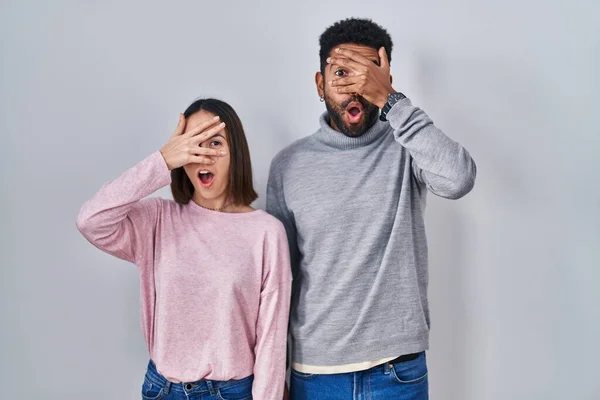 Young Hispanic Couple Standing Together Peeking Shock Covering Face Eyes — Zdjęcie stockowe