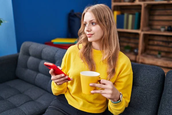 Jong Blond Vrouw Met Behulp Van Smartphone Drinken Koffie Thuis — Stockfoto