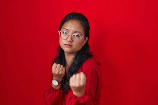 アジアの若い女性は赤い背景の上に立ち 拳の防衛ジェスチャー 怒りと動揺の顔 問題を恐れて戦う準備ができて — ストック写真