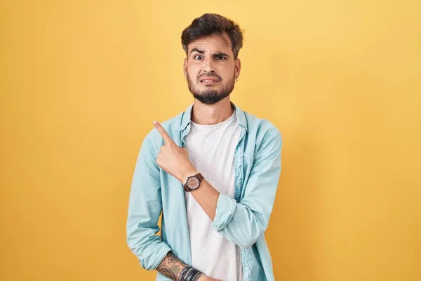 Mladý Hispánec Tetováním Stojící Nad Žlutým Pozadím Ukazuje Stranou Ustaraný — Stock fotografie