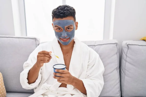 stock image Young latin man relaxed on sofa with facial mask treatment drinking coffee at home