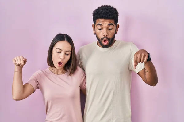 stock image Young hispanic couple together over pink background pointing down with fingers showing advertisement, surprised face and open mouth 