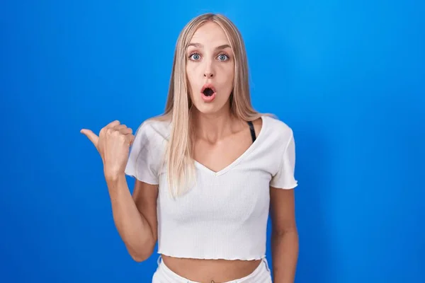 Jonge Blanke Vrouw Staande Blauwe Achtergrond Verrast Wijzend Met Hand — Stockfoto