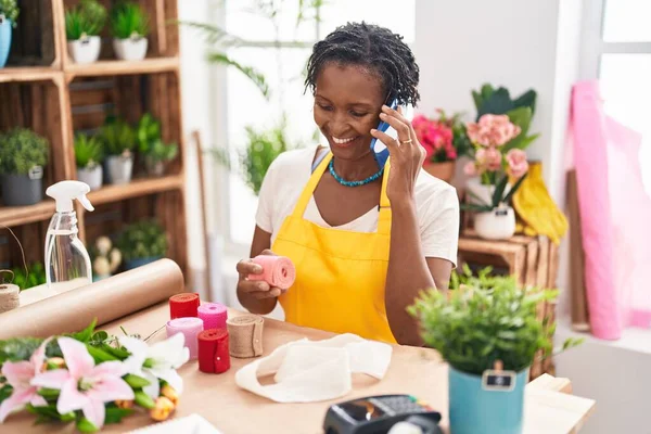 stock image Middle age african american woman florist talking on smartphone holding gift lace at flower shop