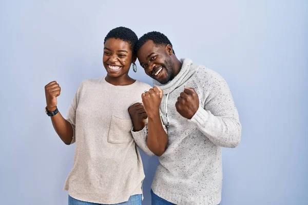 年轻的非洲裔美国夫妇站在蓝色的背景上 非常快乐而兴奋地做着获胜的手势 举起双臂 微笑着 尖叫着要成功 庆祝概念 — 图库照片