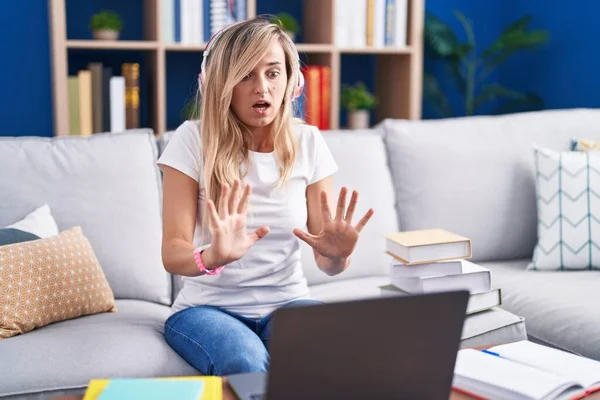 自宅でコンピュータのノートパソコンを使って勉強している若いブロンドの女性は恐怖の表情で恐怖を恐れて手でジェスチャーを止め ショックで叫んでいます パニックの概念 — ストック写真