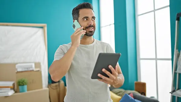 Jovem Hispânico Falando Smartphone Usando Touchpad Nova Casa — Fotografia de Stock