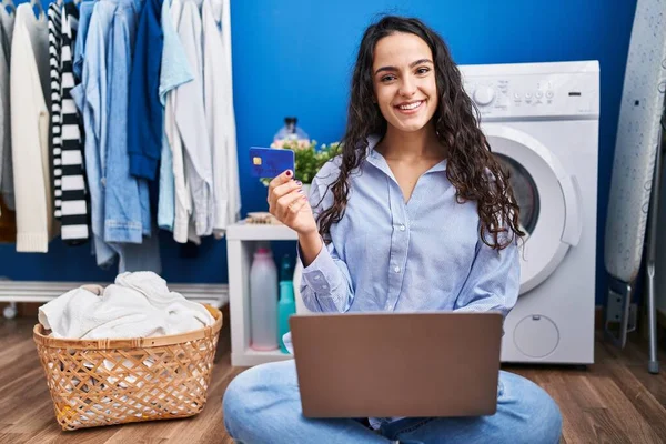 在洗衣房用手提电脑和信用卡等洗衣机的年轻女人 — 图库照片