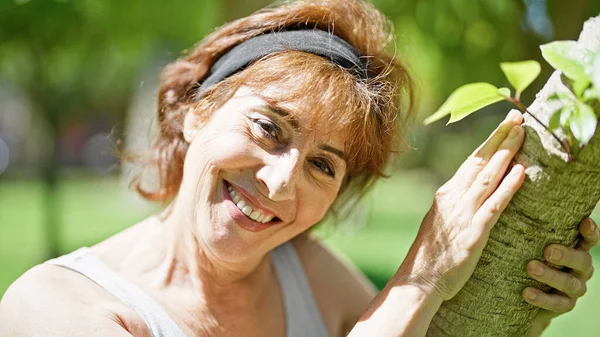 Mulher Meia Idade Sorrindo Árvore Abraçando Confiante Parque — Fotografia de Stock