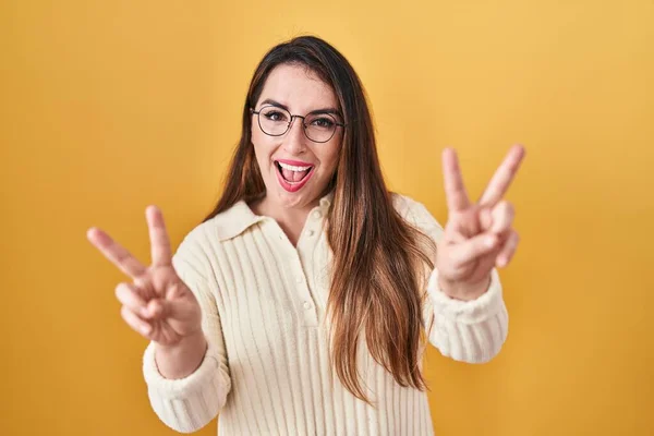 Sarı Arka Planda Durup Gülümseyen Genç Spanyol Kadın Parmaklarını Zafer — Stok fotoğraf