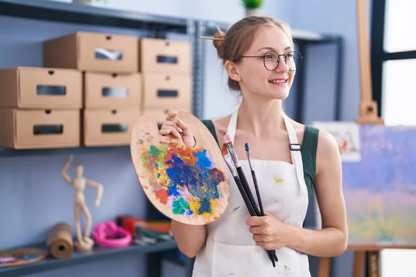 年轻的高加索女艺术家带着自信的笑容 在艺术工作室拿着画笔和调色板 — 图库照片