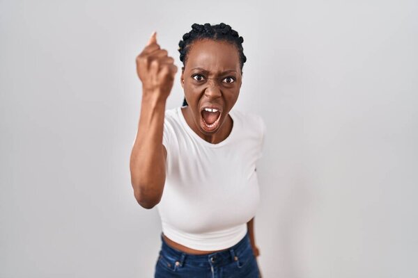 Beautiful black woman standing over isolated background angry and mad raising fist frustrated and furious while shouting with anger. rage and aggressive concept. 