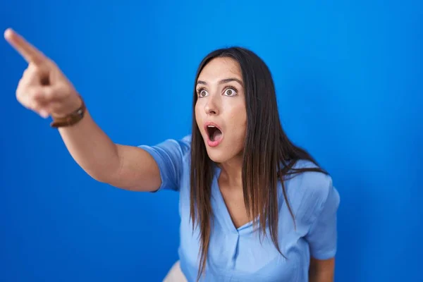 Genç Esmer Kadın Mavi Arka Planda Dikiliyor Parmağıyla Işaret Ediyor — Stok fotoğraf