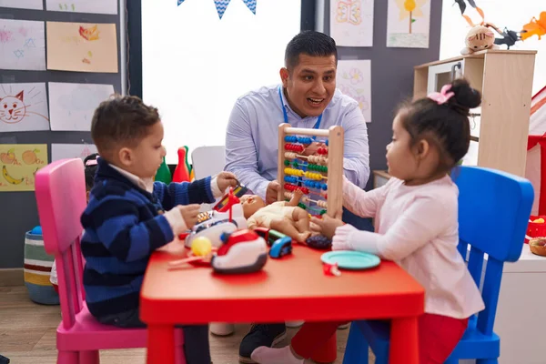 Hispanic man with boy and girl playing with abacus sitting on table at kindergarten