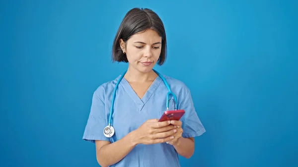 年轻美丽的惊慌失措的女医生用智能手机在孤立的蓝色背景下 — 图库照片
