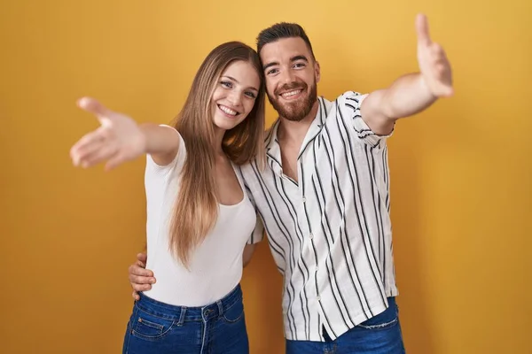 Sarı Arka Planda Duran Genç Çift Kameraya Bakıp Kucaklaşmak Için — Stok fotoğraf