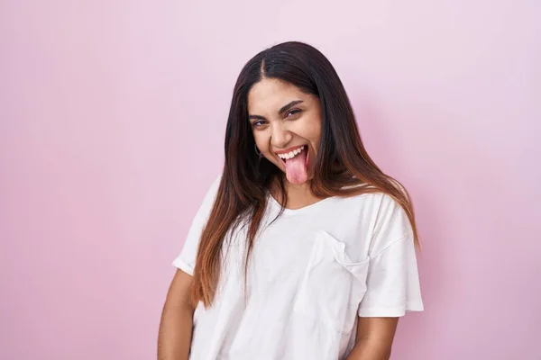 ピンク色の背景に立っている若いアラブ人女性が面白い表情で幸せ舌を突き出しています 感情の概念 — ストック写真