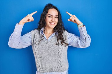 Mavi arka planda duran esmer kadın iki eliyle başını işaret ederek gülümsüyor. Harika bir fikir ya da düşünce, iyi bir hafıza. 