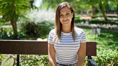 Ortadoğulu bir kadın parkta bankta otururken kendinden emin bir şekilde gülümsüyor.