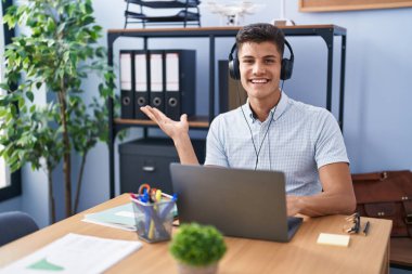 Ofiste çalışan, kulaklık takan, neşeli gülümseyen, eli avucunda kameraya bakan genç İspanyol bir adam.. 