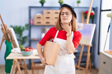 Sanat stüdyosundaki genç kızıl saçlı kadın sanat çantasını tutarken boynu ağrıyan, boğazı ağrıyan, grip, mantar ve enfeksiyon kapmış. 