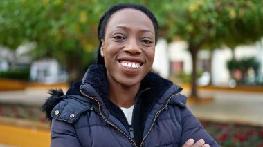 Afro-Amerikalı kadın parkta kendinden emin bir şekilde gülümsüyor.