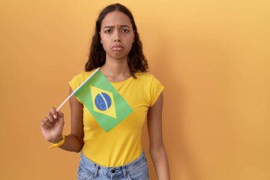 Brezilya bayrağı tutan genç İspanyol kadın üzgün ve endişeli, kızgın ve korkmuş. hüzünlü ifade. 