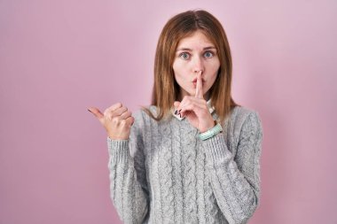 Pembe arka planda duran güzel bir kadın sessiz olmak istiyor. Parmağı dudaklarında, eli yanda. sessizlik ve gizli konsept. 