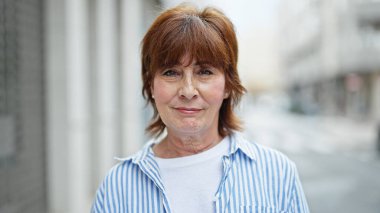 Sokakta ciddi bir ifadeyle duran orta yaşlı kadın.