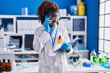 Afrika kökenli Amerikalı kadın bilim adamı laboratuvarda akıllı telefon okuyarak konuşuyor.