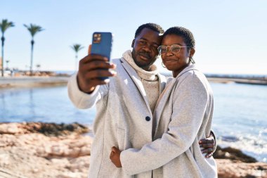 Birlikte duran erkek ve kadın deniz kenarındaki akıllı telefonun yanında selfie çekiyorlar.