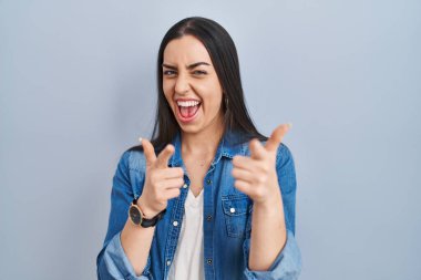 Hispanic woman standing over blue background pointing fingers to camera with happy and funny face. good energy and vibes. 
