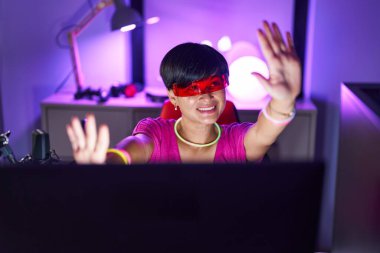 Middle age chinese woman streamer playing video game using virtual reality glasses at gaming room