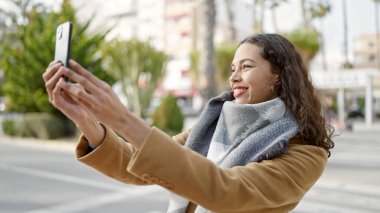 Genç ve güzel İspanyol kadın gülümsüyor. Kendine güveni tam. Sokakta akıllı telefonun yanında selfie çekiyor.