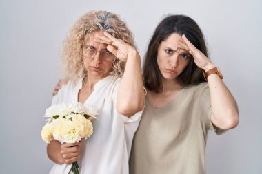 Anne ve kızı ellerinde bir buket beyaz çiçek tutuyorlar. Alnındaki bir sorun yüzünden endişeli ve stresli. Kriz için endişeli. 
