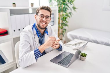 Young man doctor using laptop writing on reminder paper at clinic