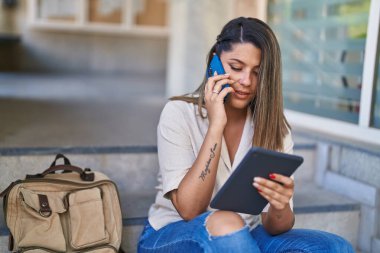 Genç İspanyol kız öğrenci üniversitede touchpad kullanarak akıllı telefondan konuşuyor.