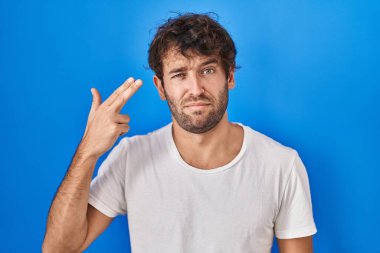 İspanyol asıllı genç adam mavi arka planda duruyor ve kendini vuruyor. Elini ve parmaklarını silah gibi kullanıyor. İntihar jesti.. 