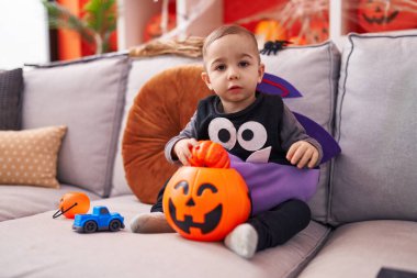 Adorable hispanic boy having halloween party holding pumpkin basket at home