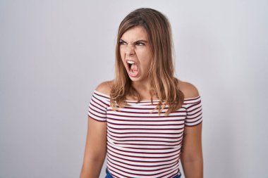 Young hispanic woman standing over isolated background angry and mad screaming frustrated and furious, shouting with anger. rage and aggressive concept. 