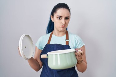 Young modern girl with blue hair wearing apron holding cooking pot skeptic and nervous, frowning upset because of problem. negative person. 