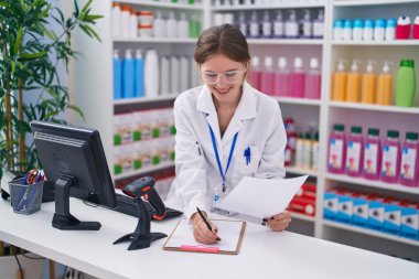 Genç sarışın eczacı eczanede panoya yazı yazıyor.