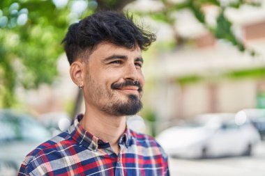 Young hispanic man smiling confident looking to the side at street