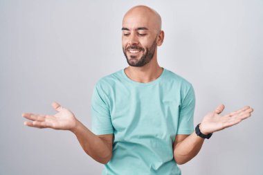 Orta yaşlı, kel bir adam beyaz arka planda gülümsüyor. İki elini de açık tutuyor. Karşılaştırma ve reklam karşılaştırması yapıyor. 