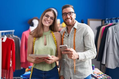 Man and woman tailors using smartphone holding notebook at clothing factory
