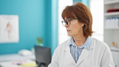 Klinikte ciddi bir ifadeyle duran orta yaşlı kadın doktor.