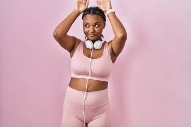 Spor kıyafetleri ve kulaklık takan, tavşan kulağı hareketi yapan, elleri avuçlarında kuşkucu ve alaycı görünen Afro-Amerikalı bir kadın. Paskalya tavşanı konsepti. 