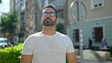 Latin kökenli genç adam ciddi bir ifadeyle sokağa bakıyor.