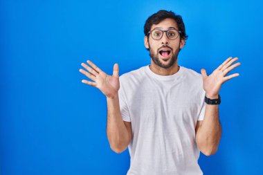 Mavi arka planda duran yakışıklı latin adam çılgın ve başarıyı kollarını kaldırıp heyecanla haykırarak kutluyor. Kazanan konsept 